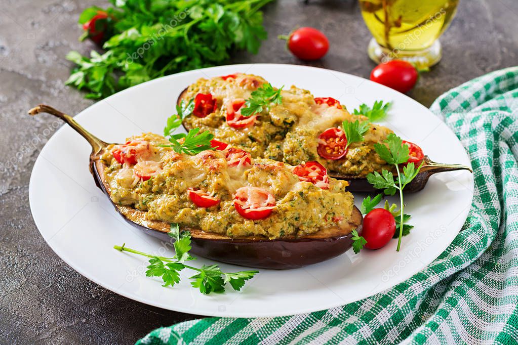 Eggplants stuffed with minced chicken meat and vegetables on white plate on grey background. 