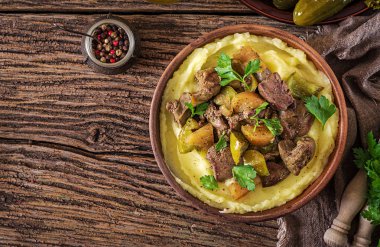 Ahşap masa üzerinde bir kasede yakın çekim olarak kızarmış tavuk karaciğer elma, tatlı biber ve soğan ile patates püresi. Üstten görünüm. Düz yatıyordu.