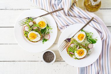 Sağlıklı gıda. Kahvaltı. Beyaz ahşap zemin üzerinde bütün tahıl ekmeği ile avokado yumurtalı sandviç. Üstten görünüm. Düz yatıyordu