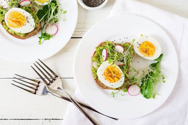 Sağlıklı gıda. Kahvaltı. Beyaz ahşap zemin üzerinde bütün tahıl ekmeği ile avokado yumurtalı sandviç. Üstten görünüm. Düz yatıyordu