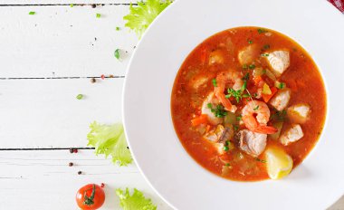 Brazilian food: Moqueca capixaba of fish and bell peppers in spicy coconut sauce  in a plate on a white wooden table. Brazilian fish stew. Top view clipart