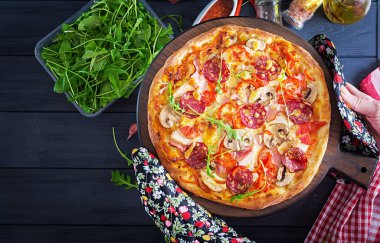 Tavuk fileto, mantar, jambon, salam, domates, peynir elinde siyah bir zemin üzerine taze İtalyan pizza. Italyan Mutfagi.