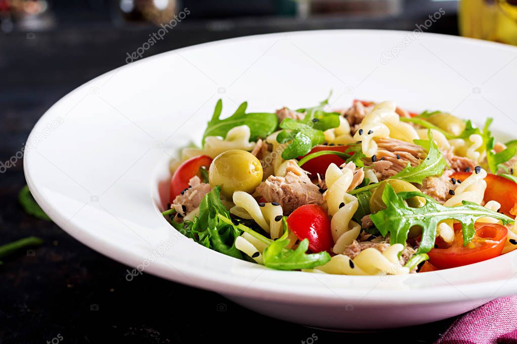 Pasta with tuna, tomatoes, olives, cucumbers, sweet pepper and arugula on rustic background 