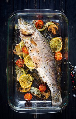 Baharatlar ve sebzeler üzerinde siyah bir arka plan ile bir pişirme çanağı içinde pişmiş levrek. Diyet menüsü. Doğru beslenme. Üstten görünüm