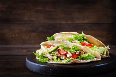 Pita ekmeği sandviç ile ızgara tavuk eti, avokado, domates, salatalık, marul üzerinde ahşap arka plan görev yaptı. Yakın çekim. Sağlıklı fast food kavramı.