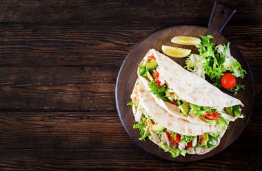 Pita ekmeği sandviç ile ızgara tavuk eti, avokado, domates, salatalık, marul üzerinde ahşap arka plan görev yaptı. Yakın çekim. Üstten Görünüm. Sağlıklı fast food kavramı.