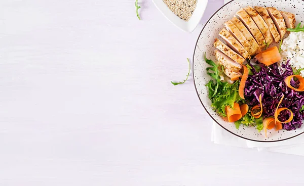 Healthy salad. Buddha bowl dish with chicken fillet, rice,  red cabbage, carrot, fresh lettuce salad and sesame. Healthy balanced eating. Top view.