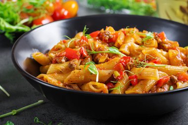 Domates, etli domates soslu Penne makarna, dekore bezelye lahanası karanlık bir tablo.