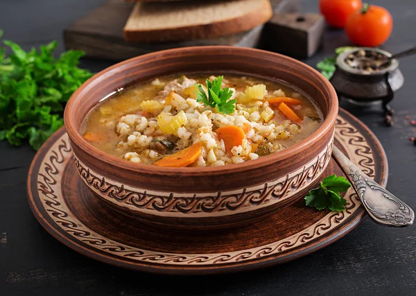 Barley soup with carrots, tomato, celery and meat on a dark background.