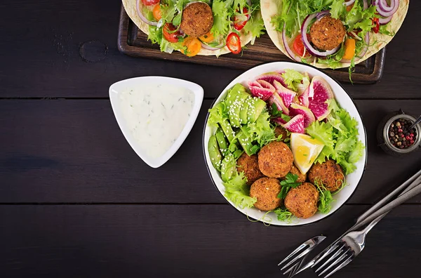 Falafel and fresh vegetables. Buddha bowl. Middle eastern or arabic dishes on a dark background. Halal food. Top view. Copy space