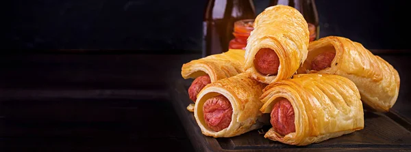 Sausage in the dough on a wooden board with tomato sauce — Stock Photo, Image