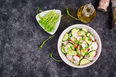 Taze sebze turp ve salatalık salatası yeşil soğan ve koyu bir arka plan üzerinde microgreens bezelye ile. Sağlıklı yiyecekler. Üst te. Kopyalama alanı.