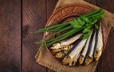 Füme sprat ve yeşil soğan ahşap bir arka plan üzerinde bir kesme tahtası üzerinde. Füme balık. Üstte görüntü