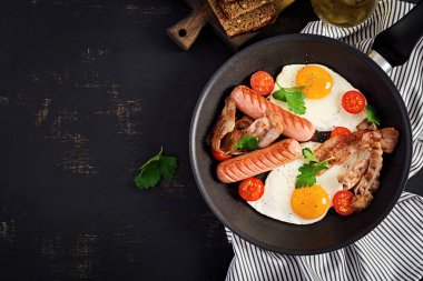 İngiliz kahvaltısı - kızarmış yumurta, domates, sosis ve pastırma. Üstte görüntü