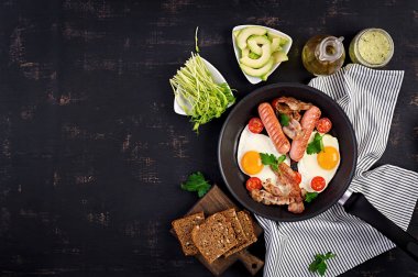 İngiliz kahvaltısı - kızarmış yumurta, domates, sosis ve pastırma. Üstte görüntü