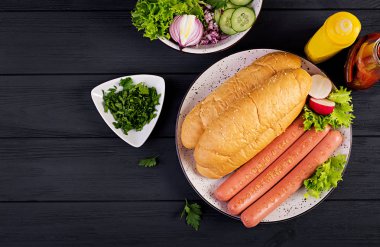 Koyu ahşap arka plan üzerinde sosis, salatalık, turp ve marul ile sosisli sandviç için Malzemeler. Yaz sosislisi. Üstte görüntü