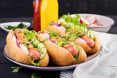 Sosis, salatalık, turp ve marul koyu ahşap arka plan üzerinde sosisli sandviç. Yaz sosislisandviçi.