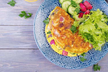 Kahvaltı. Turp, kırmızı soğan ve mavi tabakta taze salata ile Omlet. Frittata - İtalyan omlet. Üstte görüntü