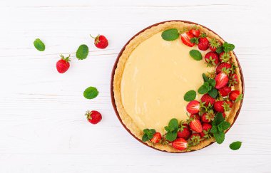 Çilek ve krem şanti hafif arka planda nane yaprakları ile süslenmiş tart. Üstte görüntü