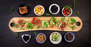 Sağlıklı vejetaryen yemek masası ayarı Düz yatıyordu. Domates, salatalık, avokado, çilek, otlar ve zeytin, aperatifler ile Sandviçler. Temiz beslenme, vegan gıda