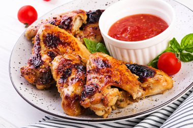 Asya tarzında pişmiş tavuk kanatları ve tabakta domates sosu.