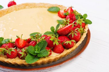 Hafif arka planda nane yaprakları ile süslenmiş çilek ve krem şanti ile Tart.