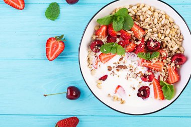 Sağlıklı kahvaltı - granola, çilek, kiraz, fındık ve yoğurt ahşap bir masada bir kase. Vejetaryen konsept gıda. Üstte görüntü