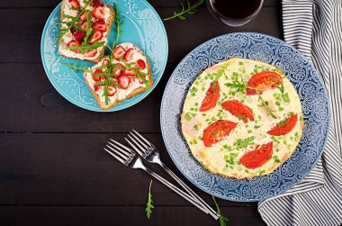 Domates, jambon, yeşil soğan ve koyu masa üzerinde çilek ile sandviç ile Omlet. Frittata - İtalyan omlet. Üstte görüntü
