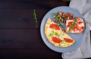 Domates, jambon, yeşil soğan ve koyu masa üzerinde çilek ile sandviç ile Omlet. Frittata - İtalyan omlet. Üstte görüntü