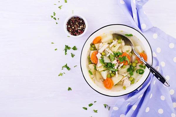 Chicken soup with green peas, carrots and potatoes in a white bowl on a light background. Top view