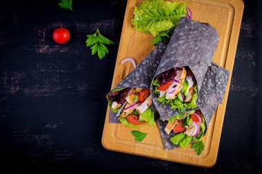 Tortilla ile eklenen mürekkep mürekkepbalığı siyah arka planda tavuk ve sebze ile sarar. Tavuk burrito, Meksika yemeği. Üst görünüm