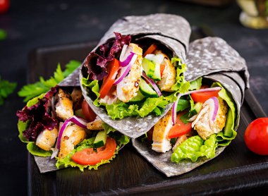 Tortilla ile eklenen mürekkep mürekkepbalığı siyah arka planda tavuk ve sebze ile sarar. Tavuk burrito, Meksika yemekleri.