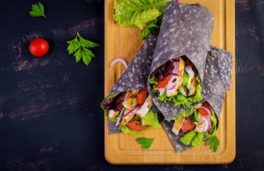 Tortilla ile eklenen mürekkep mürekkepbalığı siyah arka planda tavuk ve sebze ile sarar. Tavuk burrito, Meksika yemeği. Üst görünüm