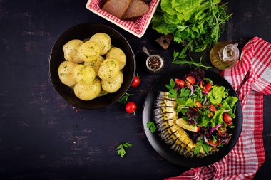 Füme uskumru, haşlanmış patates ve karanlık arka planda taze salata. Üst görünüm