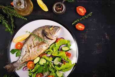 Koyu rustik arka plan üzerinde beyaz tabakta limon ve taze salata ile Fırında balık dorado. Üst te. Balık konsepti ile sağlıklı bir akşam yemeği. Diyet ve temiz beslenme