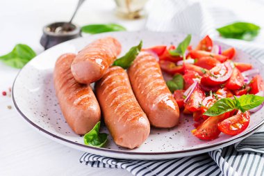 Domates, fesleğen salatası ve kırmızı soğan ile ızgara sosis. Barbekü menüsü.