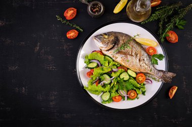 Koyu rustik arka plan üzerinde beyaz tabakta limon ve taze salata ile Fırında balık dorado. Üst te. Balık konsepti ile sağlıklı bir akşam yemeği. Diyet ve temiz beslenme