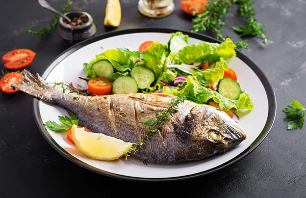 烤鱼多拉多柠檬和新鲜的沙拉在黑暗的质朴背景的白色盘子 健康晚餐与鱼的概念 饮食和清洁饮食 — 图库照片