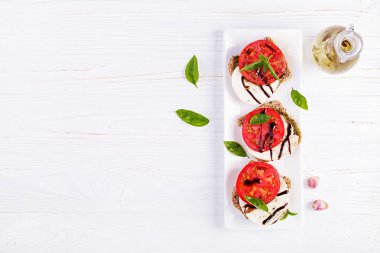 Beyaz ahşap masa üzerinde mozzarella, domates ve çavdar ekmeği ile Sandviçler. Üstte görüntü