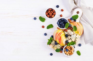 Çeşitli peynirler, yaban mersini, elma, beyaz masada fındık ile peynir tabağı. İtalyan peynir tabağı ve meyve. Üst görünüm, genel merkez