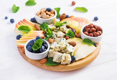 Cheese platter with assorted cheeses, blueberry, apples, nuts on white table. Italian cheese  platter and fruit. clipart