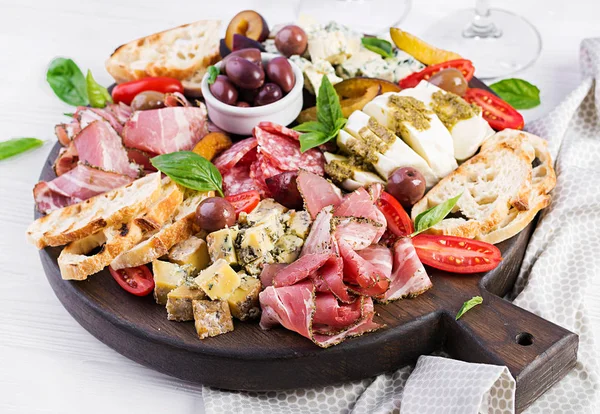 Antipasto platter with ham, prosciutto, salami, blue cheese, mozzarella with pesto and olives on a wooden background.