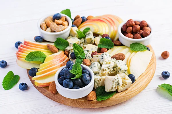 Cheese platter with assorted cheeses, blueberry, apples, nuts on white table. Italian cheese  platter and fruit.