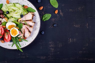 Ketojenik diyet. Keto brunch' ı. Haşlanmış yumurta, domuz biftek ve zeytin, salatalık, ıspanak, brie peyniri, fındık ve domates. Üstte görüntü