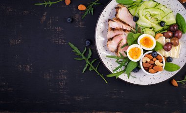 Ketojenik diyet. Keto brunch' ı. Haşlanmış yumurta, domuz biftek ve zeytin, salatalık, ıspanak, brie peyniri, fındık ve yaban mersini. Üstte görüntü