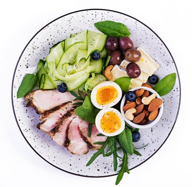 Ketojenik diyet. Keto brunch' ı. Haşlanmış yumurta, domuz biftek ve zeytin, salatalık, ıspanak, brie peyniri, fındık ve yaban mersini. Üstte görüntü