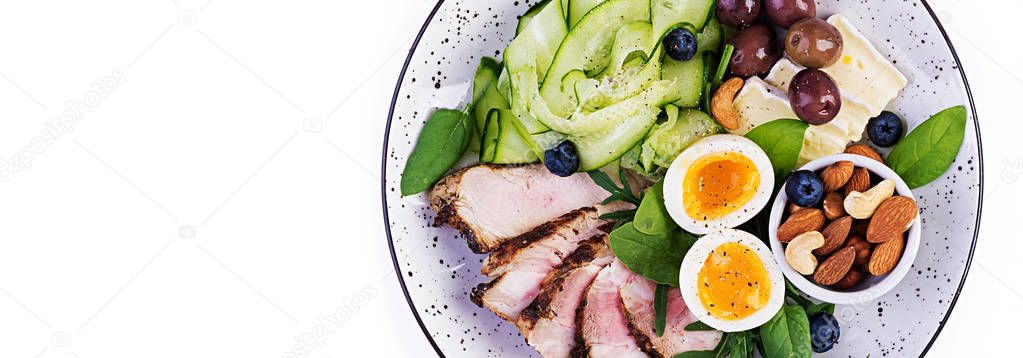 Ketogenic diet. Keto brunch. Boiled egg, pork steak and olives, cucumber, spinach, brie cheese, nuts and blueberry. Banner. Top view