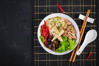 Tofu peyniri ile Asya vegan erişte çorbası, shimeji mantar ve koyu arka plan üzerinde kase kızarmış patlıcan. Üstte görüntü