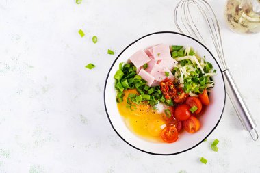 Omlet malzemeleri: yumurta, jambon, domates, yeşil otlar, ışık masasında süt ve peynir. Üst görünüm, genel görünüm, düz görünüm