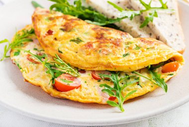 Domatesli omlet, jambon, peynir ve tabakta yeşil otlar. Frittata - İtalyan omleti.